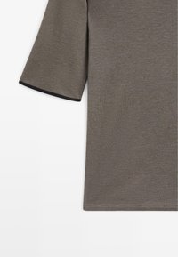 Grijs t-shirt met korte mouwen en een geribbelde structuur. Voorzien van een zwarte bies langs de mouwranden. Gladde stof met een nette afwerking.