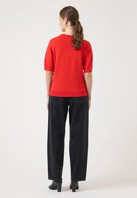 Rød kortermet strikket topp med ribbet kant, kombinert med høytlivs svarte vide jeans og svarte ankelstøvler med hæl.