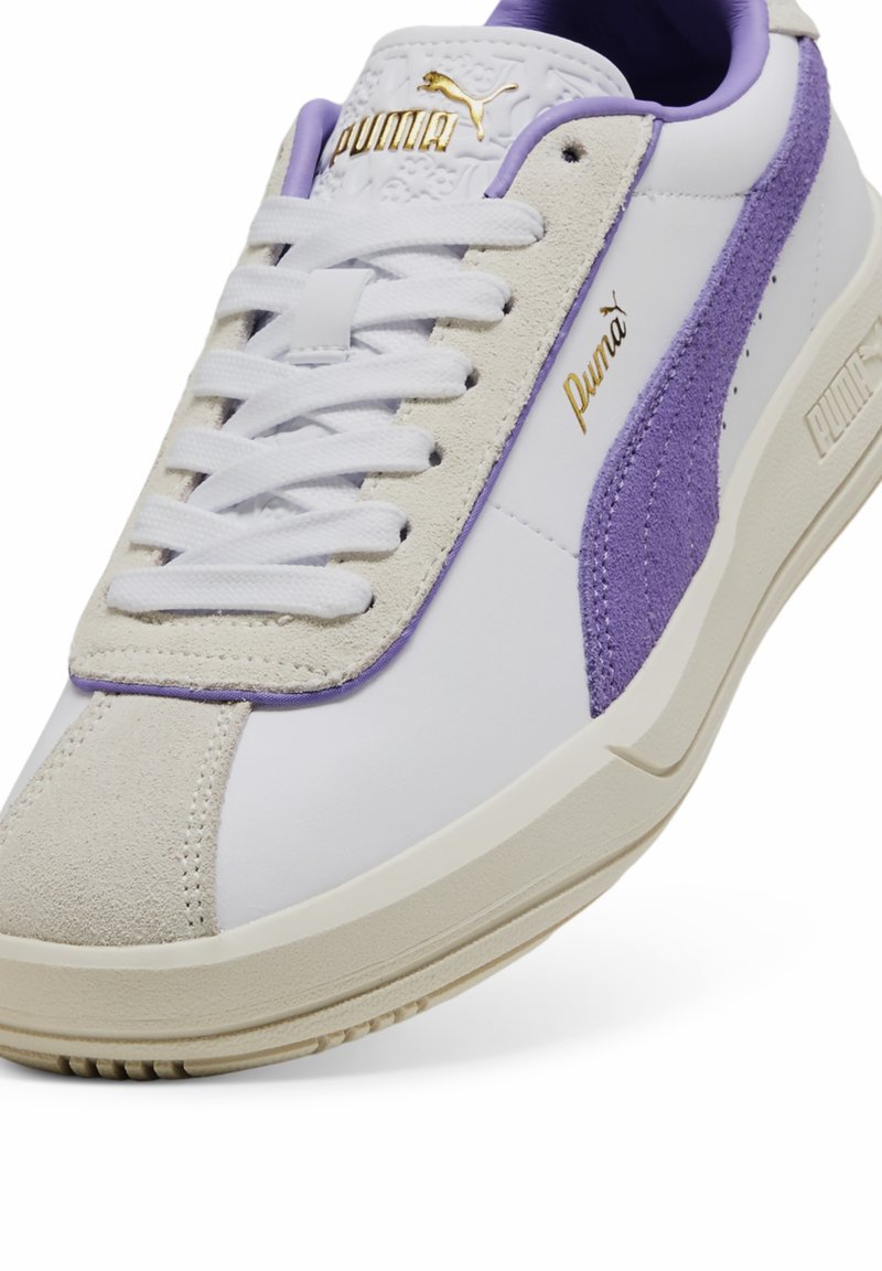 Weiße Leder-Sneaker mit lila Wildlederakzenten, Creme-Zwischensohle und goldenem Puma-Logo. Verfügt über ein Schnürdesign und strukturierte Details an der Zunge.
