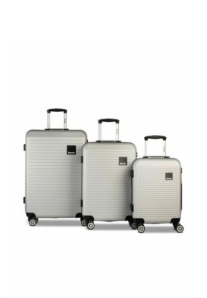 Trois valises rigides argentées avec quatre roues et poignées télescopiques, disposées du plus grand au plus petit, avec un logo Bench noir.