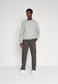 Grå sweatshirt med rund hals, kombinert med mørke cargo-bukser med knapper på sidene og lommer. Fullført med hvite joggesko.