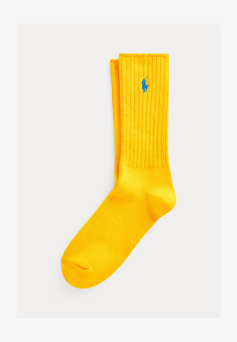 Φωτεινό κίτρινο ριμπ κάλτσα με ένα μικρό μπλε κεντητό λογότυπο κοντά στην κορυφή, απεικονισμένη σε απλό λευκό φόντο.