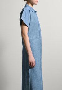 Vestito in chambray a maniche corte con colletto, caratterizzato da una silhouette dritta, spacchi laterali e una texture di tessuto azzurro chiaro.