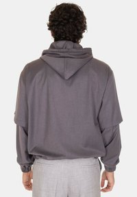Felpa grigia con cappuccio e vestibilità rilassata, caratterizzata da maniche ampie e polsini elastici. Texture liscia, design minimalista, senza loghi visibili.