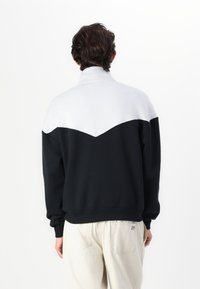 Fleece sweatshirt i svart och vitt med färgblockering, hög krage och sned vit panel. Mjuk textur; avslappnad passform; ribbade manschetter och nederkant.