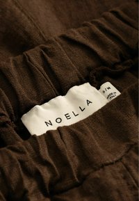 Tissu avec ceinture élastique marron avec étiquette blanche indiquant "NOELLA S/M Fabriqué en Italie."