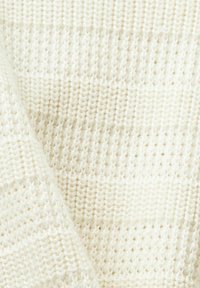 Gros plan sur un tissu tricoté blanc doux avec des points visibles et un motif texturé.