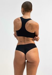 Top sportivo nero con scollatura alta e spalline larghe, abbinato a slip bikini neri coordinati. Tessuto liscio e elastico e design minimal.