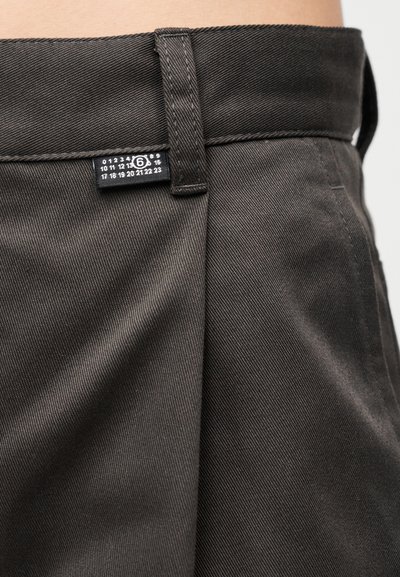 Calças castanhas com tecido texturizado, apresentando uma cintura visível e uma etiqueta de tamanho no interior.