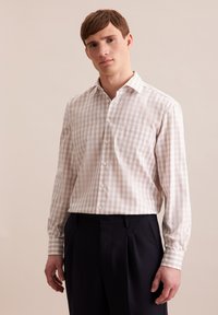 Camicia a quadri beige e bianca, maniche lunghe, colletto con bottoni, con tasca frontale e pantaloni scuri a contrasto. Tessuto liscio e leggero.