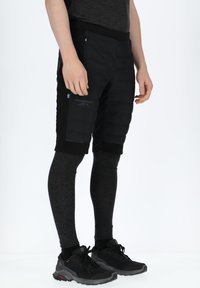 Sorte polstrede shorts med en lynlås lomme, parret med mørkegrå leggings. Har et logo på shortsene og et strømlinet, moderne design.