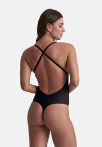 Costume da bagno intero nero con schiena bassa e spalline incrociate. Tessuto liscio e design minimalista con apertura alta sulle gambe.