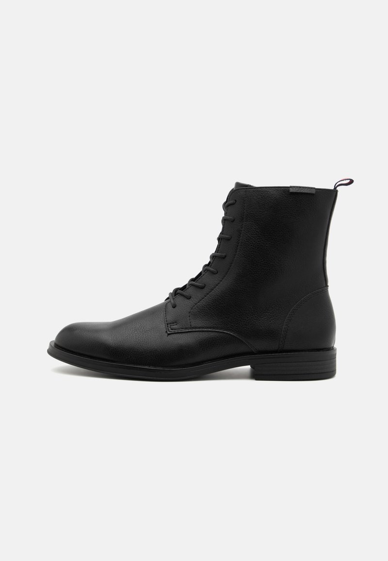 Bota de tobillo de cuero negro con Punta redonda, parte superior texturizada, cordones laterales y una pestaña en el talón. Suela plana con un tread sutil.