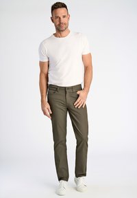 T-shirt blanc ajusté, pantalon slim-fit vert olive et baskets blanches. Le pantalon dispose d'une braguette zippée et de poches, avec une légère texture dans le tissu.