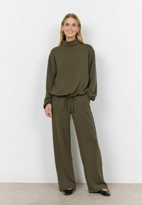 Olivgrön loungewear-set med en höghalsad tröja med långa ärmar och löst sittande byxor med dragsko. Mjuk textur, minimalistisk design.