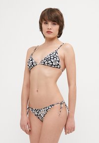 Tengerés fekete bikini virágmintás krémszínből; háromszög alakú felső vékony pántokkal, hozzáillő, alacsony derékú alsó rész oldalra kötözőkkel. Sima anyag textúra.
