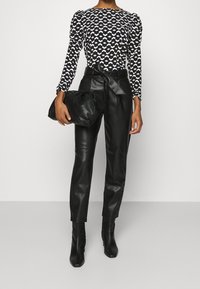 Černobíle vzorovaná halenka s dlouhým rukávem a balónovými rameny, spárovaná s černými koženými kalhotami s vysokým pasem a černou skládací kabelkou.