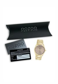 Montre-bracelet en or avec un cadran rond marron, bracelet en métal et design minimaliste. Comprend une boîte d'emballage noire et une carte de garantie.