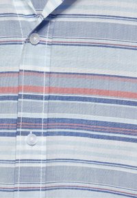 Košile na knoflíky s vodorovnými pruhy ve světle modré, námořnické a červené barvě. Materiál se zdá být lehký s hladkým povrchem. Viditelný detail jednoho knoflíku.