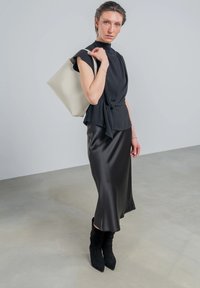 Schwarzes Satin-Kleid kombiniert mit einem figurbetonten schwarzen Oberteil und einer beigen Tragetasche. Das Modell trägt schwarze kniehohe Stiefel. Glatte Texturen und maßgeschneiderte Designs.
