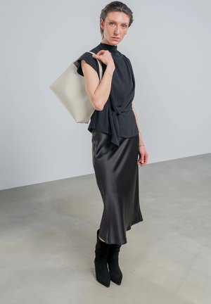 Robe en satin noir associée à un haut noir ajusté et à un sac fourre-tout beige. Le modèle porte des bottes noires jusqu'aux genoux. Textures lisses et design épuré.