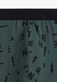 Zielone bokserki z czarnym elastycznym paskiem w talii. Posiadając powtarzający się czarny wzór tekstu oraz gładką fakturę materiału.