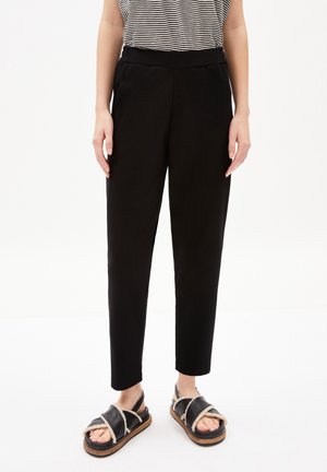 Pantaloni neri a gamba affusolata in tessuto morbido con vita elasticizzata, abbinati a sandali neri con suola spessa e un accentuato cinturino crema.