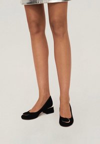 Pumps in pelle scamosciata nera con tacco a blocco, caratterizzati da una punta arrotondata con un accento metallico. Il design include un collo del piede basso per un aspetto elegante.