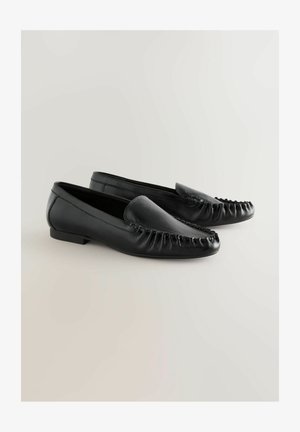 Mocasines de cuero negro con punta redondeada, con un diseño fruncido a lo largo del borde y un tacón bajo y cuadrado. Textura lisa en toda la superficie.
