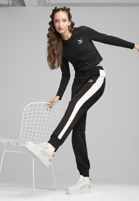 Čierny crop top s dlhým rukávom s logom Puma, čierne nohavice na jogging s bielymi bočnými pruhmi a biele platformové tenisky. Minimalistický dizajn.