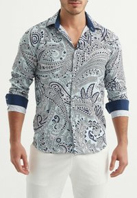 Chemise bleu clair à manches longues avec un motif paisley bleu marine. Col et poignets bleu marine contrastants, avec un tissu texturé et un design à boutons sur le devant.