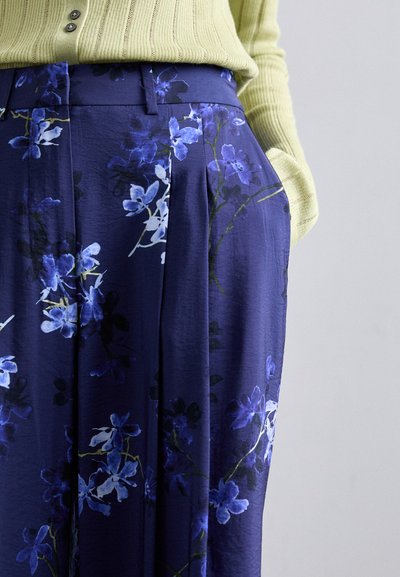 Floral print trousers in navy with blue and white flowers. Features a high waist, pleats, and side pockets; fabric appears lightweight and smooth.