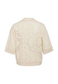 Blusa di colore crema chiaro con ricami tonali intricati e bordo di pizzo scallopato sulle maniche. Presenta una vestibilità ampia e rilassata con maniche corte.