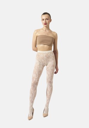 Kvinde iført nude bandeau top, hvide blomster-lace strømpebukser og beige høje hæle, stående mod en ensfarvet lysegrå baggrund.