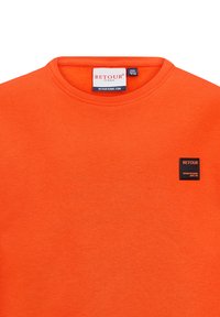 Felpa arancione con collo rotondo, colletto a costine e piccolo etichetta nera "RETOUR" sul davanti. Il tessuto appare morbido e texturizzato.