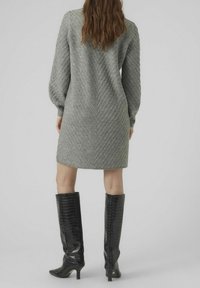 Robe grise en tricot avec un motif chevron texturé, manches longues et corsage cintré. Associée à des bottes noires en cuir verni montantes jusqu'aux genoux.