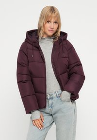 Chaqueta acolchada burdeos con capucha, forma cuadrada, diseño de acolchado horizontal, cierre de cremallera y cordón ajustable en un entorno casual.