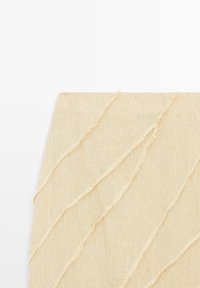 Tissu texturé beige présentant des lignes ondulées et des bords effilochés, créant un aspect superposé. Matériau lisse avec un éclat subtil.