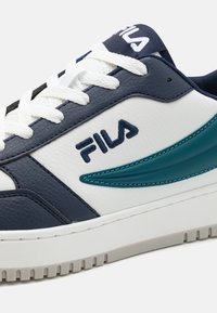 Fila tenisice s gornjim dijelom od tamnoplave kože, bijelom kožom na dnu, akcentom u tirkiznoj boji i teksturiranom gumiranom potplatom. Ima bijele vezice i logo.