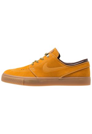 Baskets basses en daim jaune moutarde avec semelle en gomme, lacets à l’avant et logo Nike Swoosh discret sur le côté.
