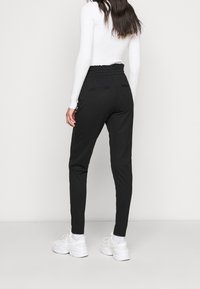 Černé zúžené tepláky s elastickým pasem a plochými předními kapsami, spárované s bílým přiléhavým tričkem s dlouhým rukávem a bílými teniskami.