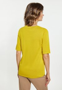 Gul kortærmet top med rund hals, ribbet tekstur og en afslappet pasform, parret med beige bukser. Glat stof uden grafik.