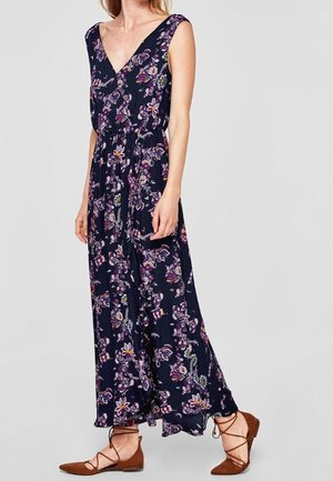 Granatowa sukienka maxi bez rękawów z różowo-białym kwiatowym wzorem, dekoltem w kształcie litery V i talią podkreśloną paskiem, noszona z brązowymi, sznurowanymi balerinami.