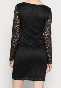 Robe en dentelle noire avec des manches longues ornées d'un motif en dentelle complexe, corsage ajusté et jupe fluide, mettant en avant un design texturé.