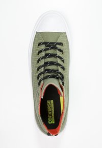 Sneaker verde in tela con motivo testurizzato, punta in gomma bianca, lacci neri con macchie bianche e dettagli arancioni all'interno.