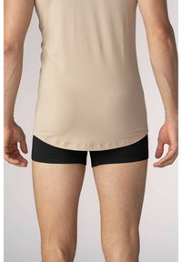 Beige, figurnära linne med en slät yta, tillsammans med svarta, tighta shorts. Synlig sömnad längs kläddets kanter.