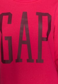 Felpa fucsia con grande logo "GAP" marrone scuro. Realizzata in morbido cotone, presenta un classico collo rotondo e una vestibilità morbida.