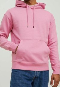 Rosa huvtröja med framficka, dragsko och ribbade mudd. Tyget ser mjukt och texturerat ut. Bärs tillsammans med blå jeans.