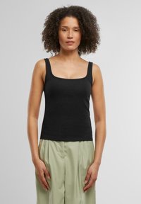 Top de tirantes ajustado y negro hecho de un material acanalado. Presenta un escote cuadrado y tirantes anchos, combinado con pantalones de color verde claro.
