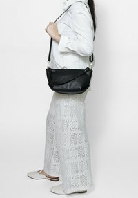 Zwarte leren crossbody tas met een gestructureerd oppervlak, gebogen vorm, zilveren hardware-accenten en een lange verstelbare schouderband.